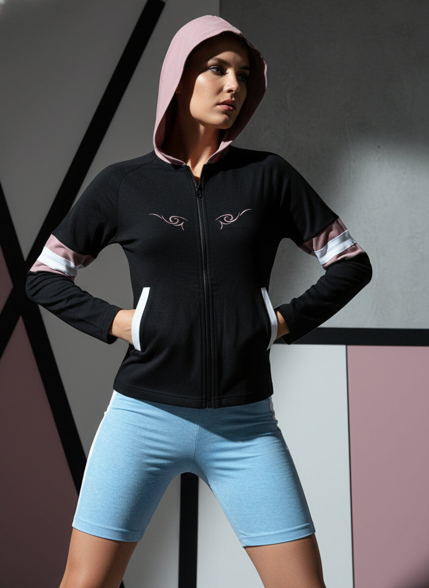 Person wearing a black hoodie with pink hood and white accents, paired with light blue shorts against a geometric background.