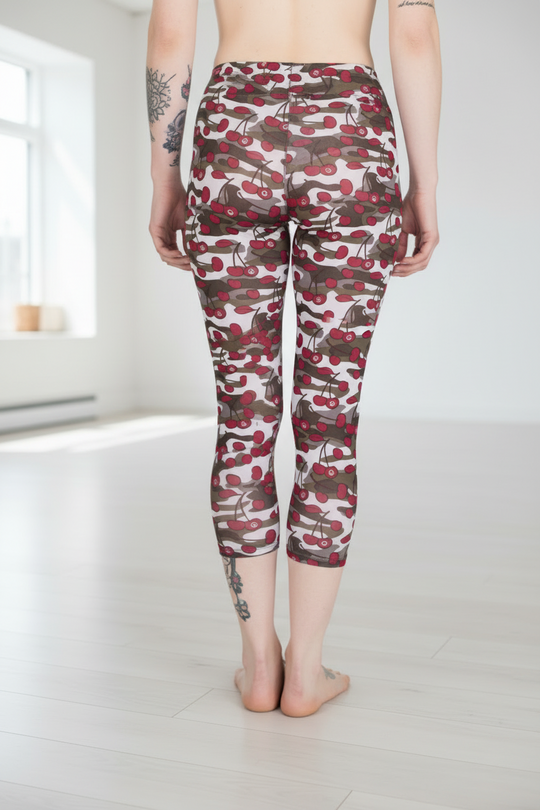 A person wearing high-waisted cropped leggings with a red, brown, and white camouflage pattern, standing barefoot in a bright, minimalist room with light wood floors.